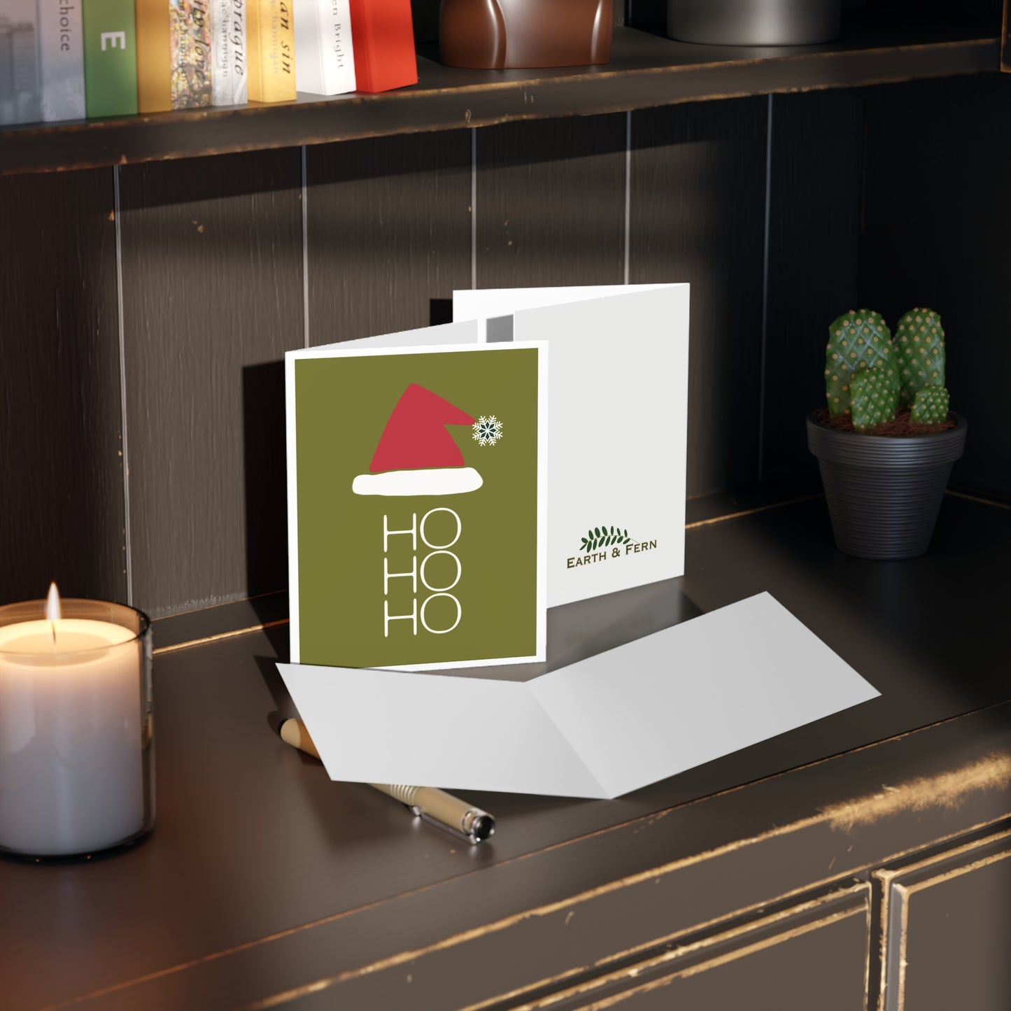 Mockup of holiday greeting card displaying the front design with a chartreuse green background, a red Santa hat with a snowflake pom pom, and 'Ho, Ho, Ho' written in white, blank inside, and company logo on the back