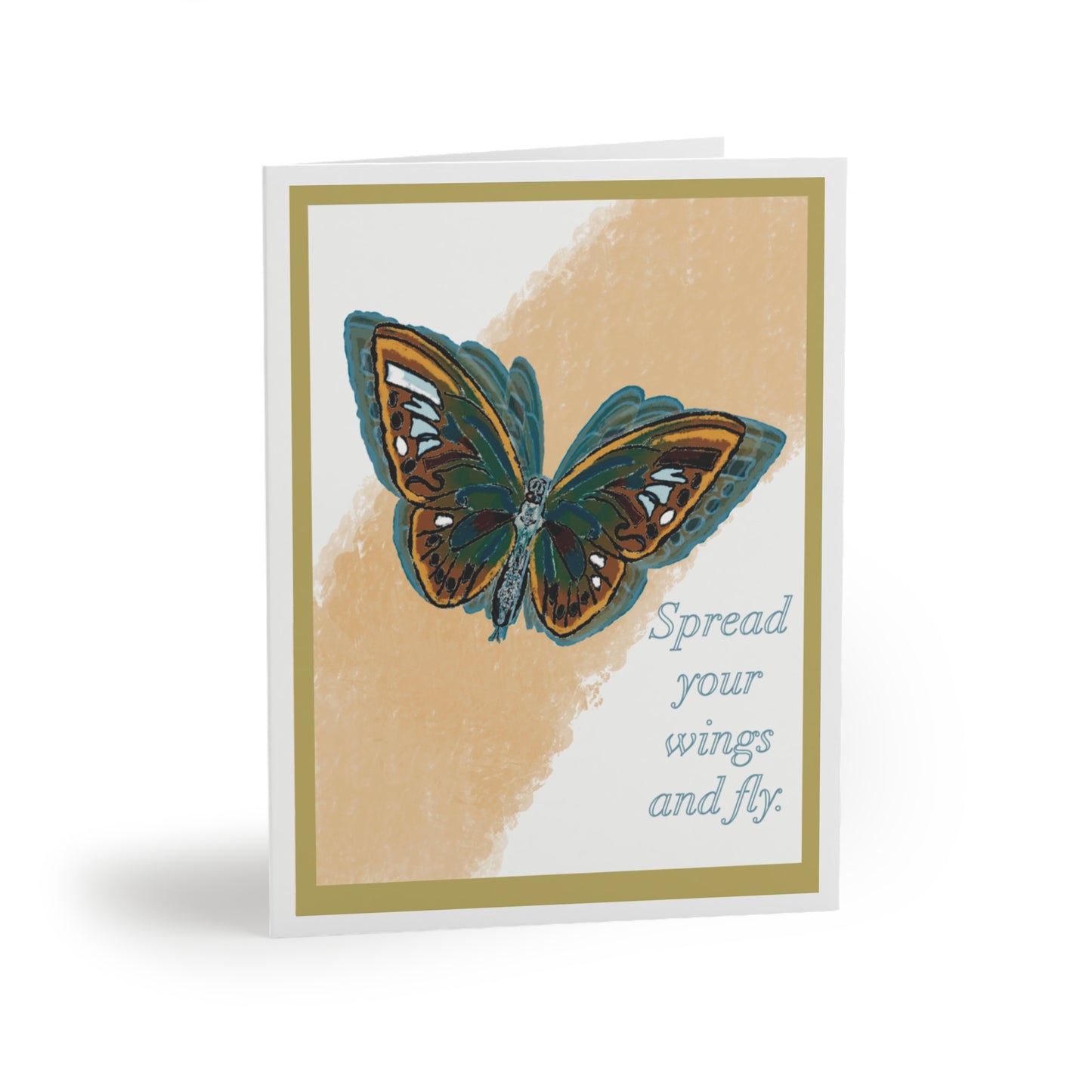 The image shows the front of the greeting card. On it is a Blue, yellow, orange and brown butterfly in flight. Behind is is a streak of faded light orange in its flight path. The background is white with a sage and white double border. The words “Spread your wings and fly” are written on the card.