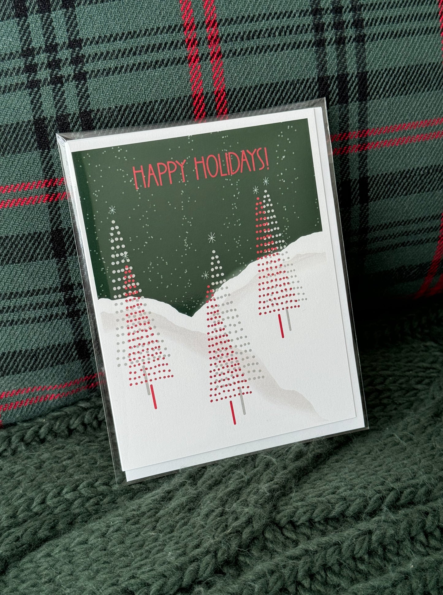Charming greeting card featuring a trio of pencil Christmas trees set against a snowy landscape, with a night sky and light snowflakes falling, and the words 'Happy Holidays' elegantly displayed near the top."