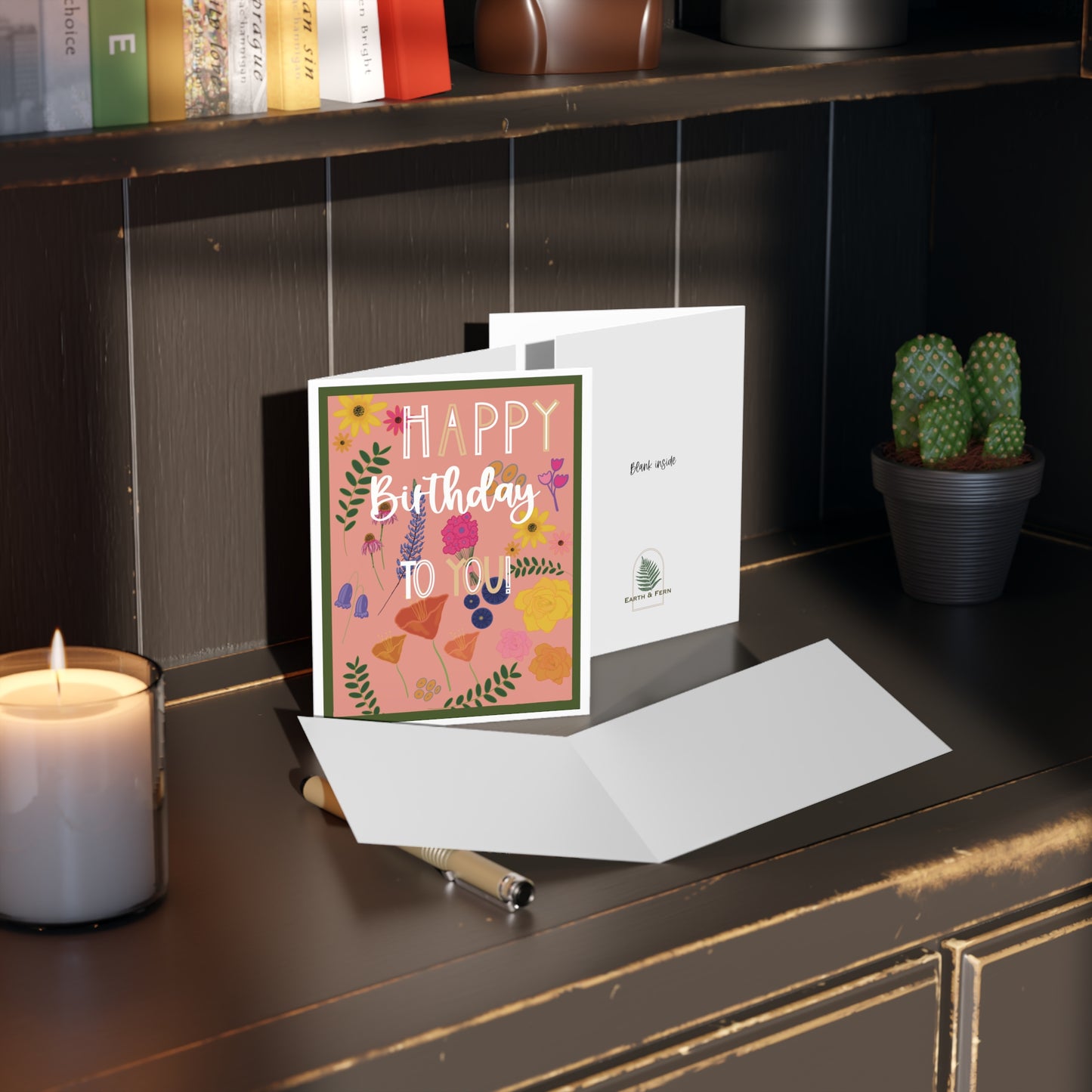 Mockup of birthday greeting card displaying the front design with a pink background and multicolor floral pattern, blank inside, and company logo on the back.