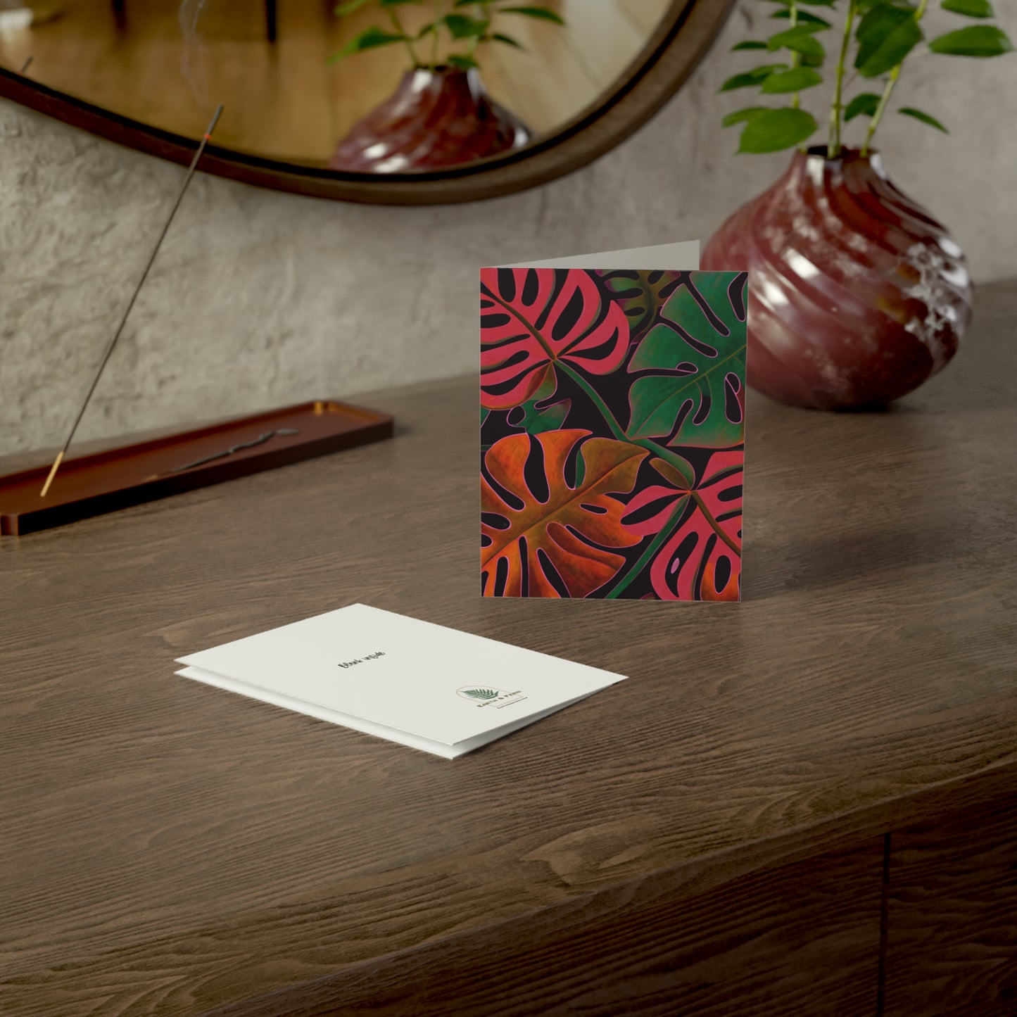 Mockup of Holiday Monstera Greeting Card set showing the front, blank inside, and back. The front features a vibrant tropical Monstera leaf design with holiday colors. The inside is blank for a personalized message. The back showcases the Earth & Fern logo with the words 'Blank Inside.