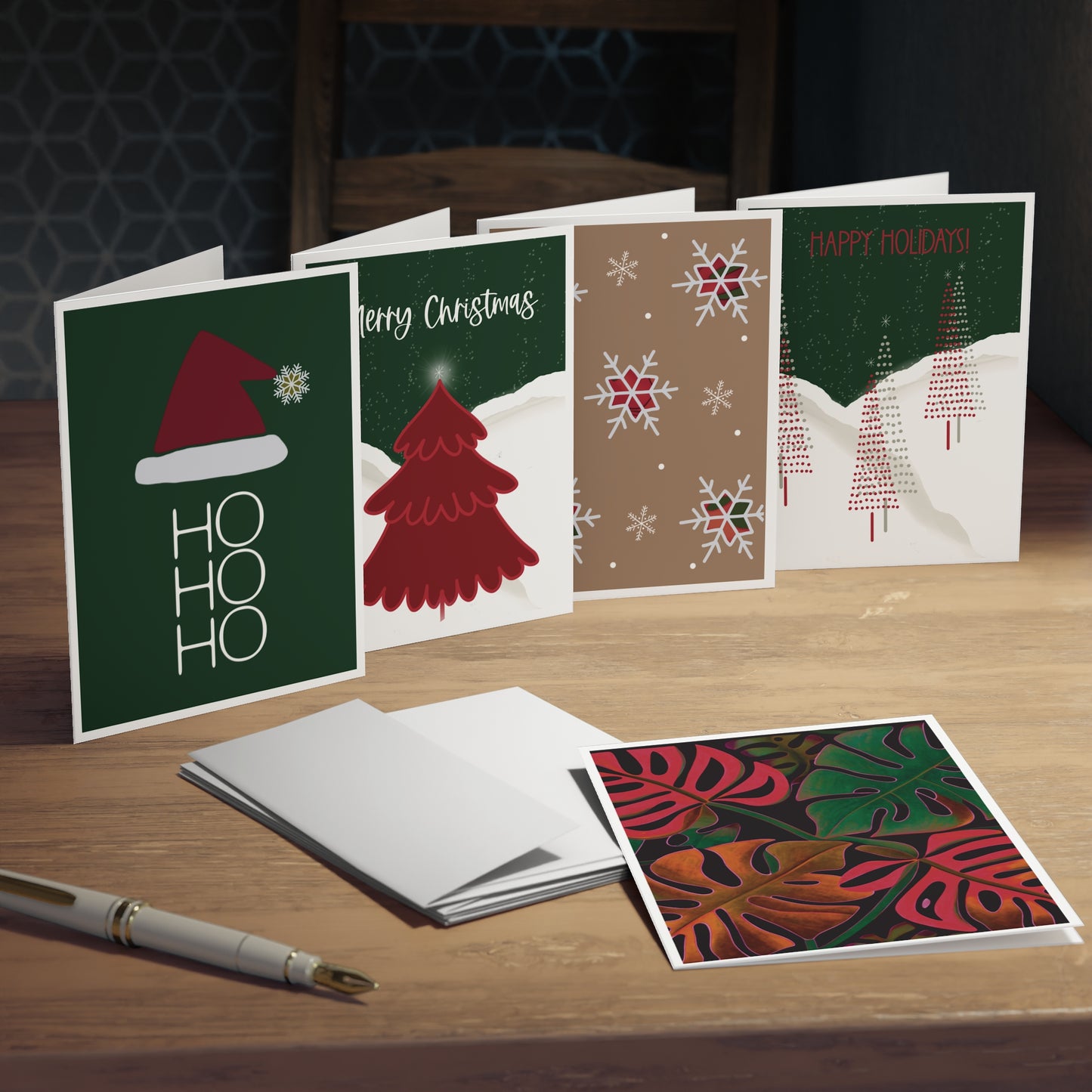 Mockup of a set of five mixed greeting cards displaying the front designs, showing a monstera plant, Santa hat with 'Ho, Ho, Ho,' night sky with a red tree, tan card with snowflakes and plaid, and night sky with skinny pencil Christmas trees. The mockup also includes the backs and blank insides of each card. With white envelopes