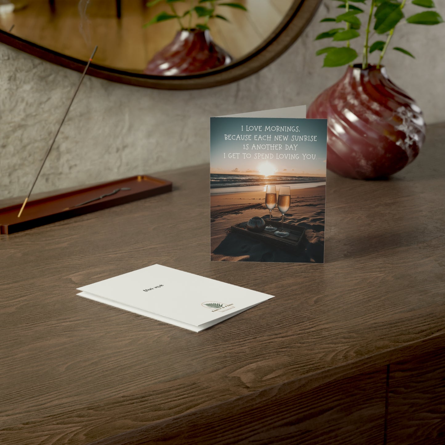 A romantic greeting card featuring a sunrise, two glasses of champagne on a beach blanket, and the message "I love mornings, because each new sunrise is another day I get to spend loving you.