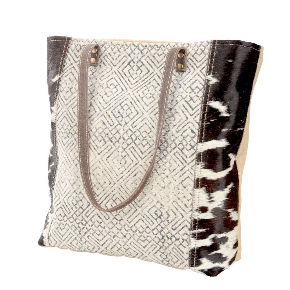 Black and cream geometric design tote with dark brown leather straps and cowhide accents. Stylish and eco-friendly, perfect for everyday use or as a statement accessory