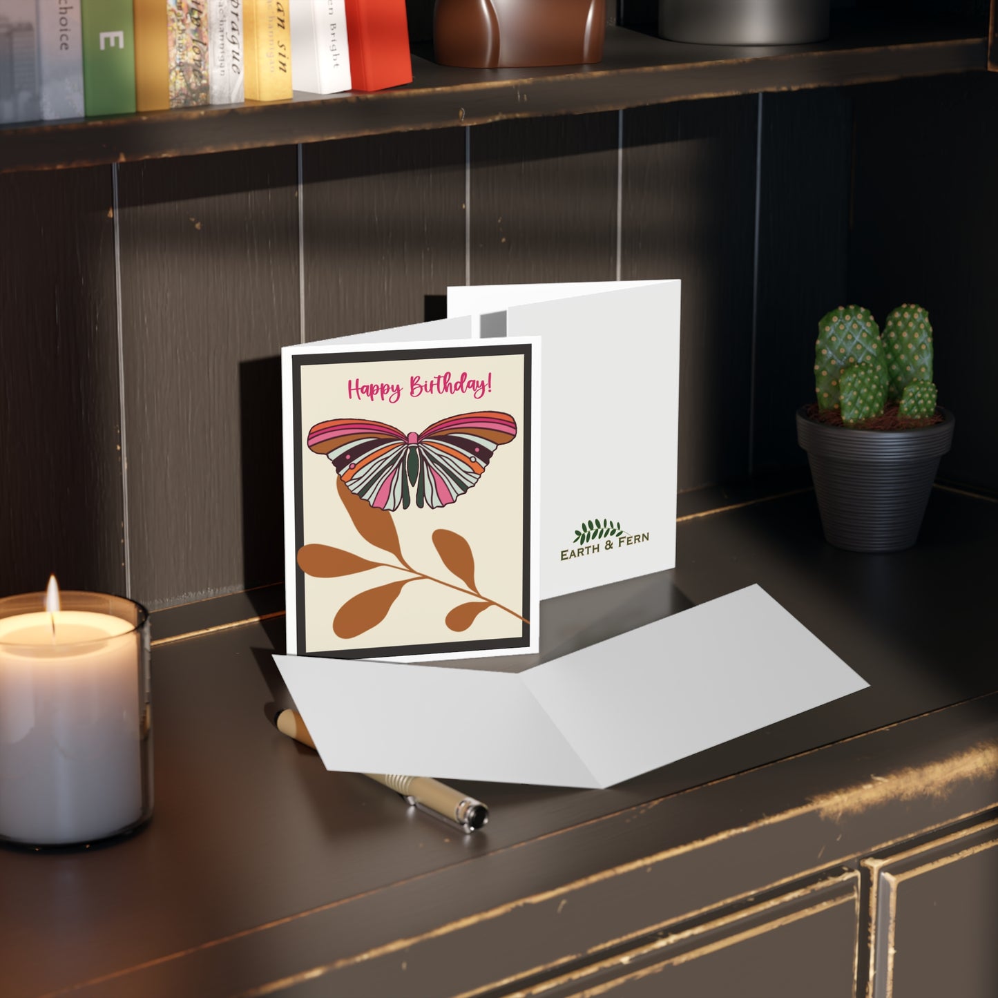 Mockup of greeting card displaying the front design with a colorful butterfly on a cream background and black border, blank inside, and company logo on the back