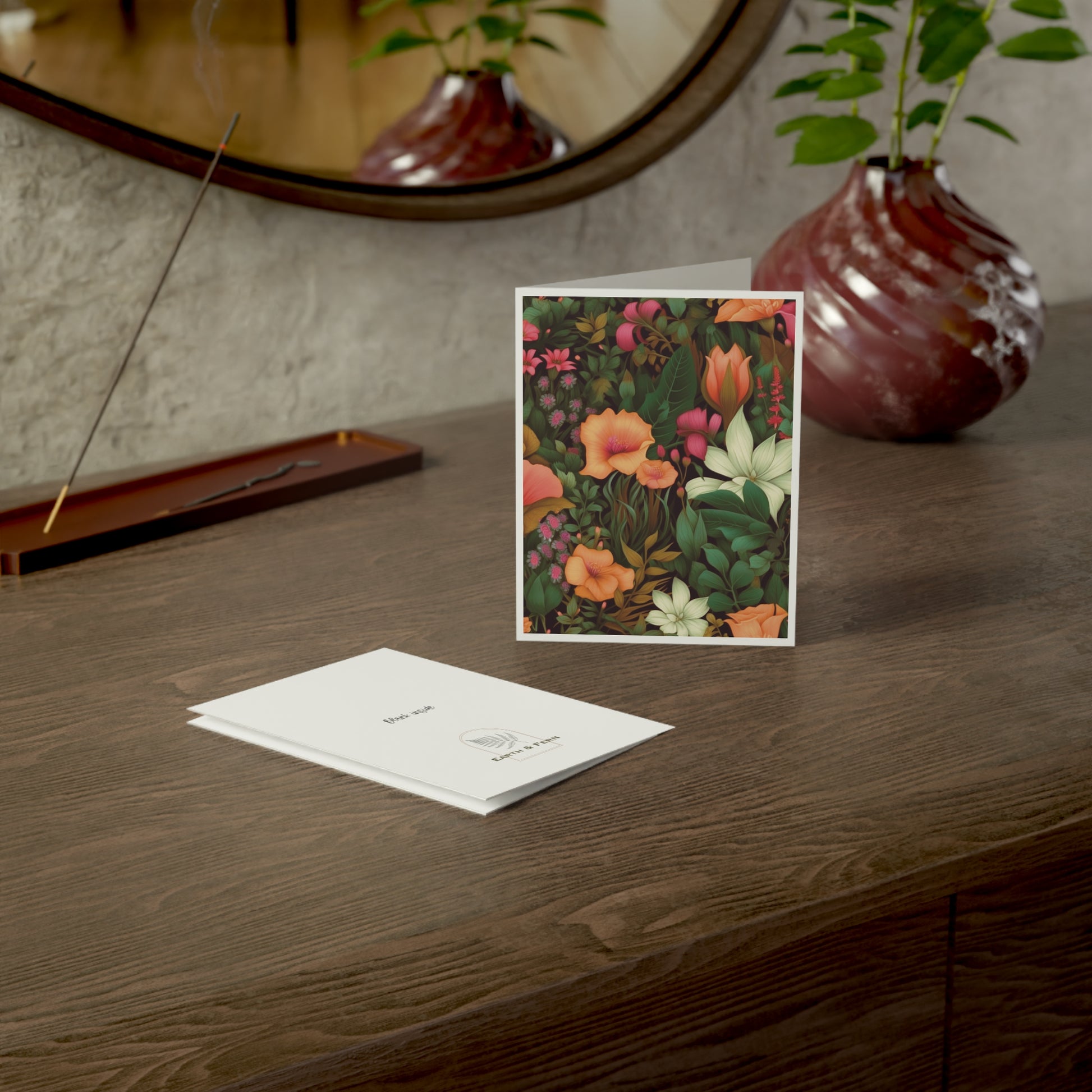 Mockup of daylily floral greeting card displaying the front design with vibrant green, pink, orange, and white flowers, blank inside, and company logo on the back.