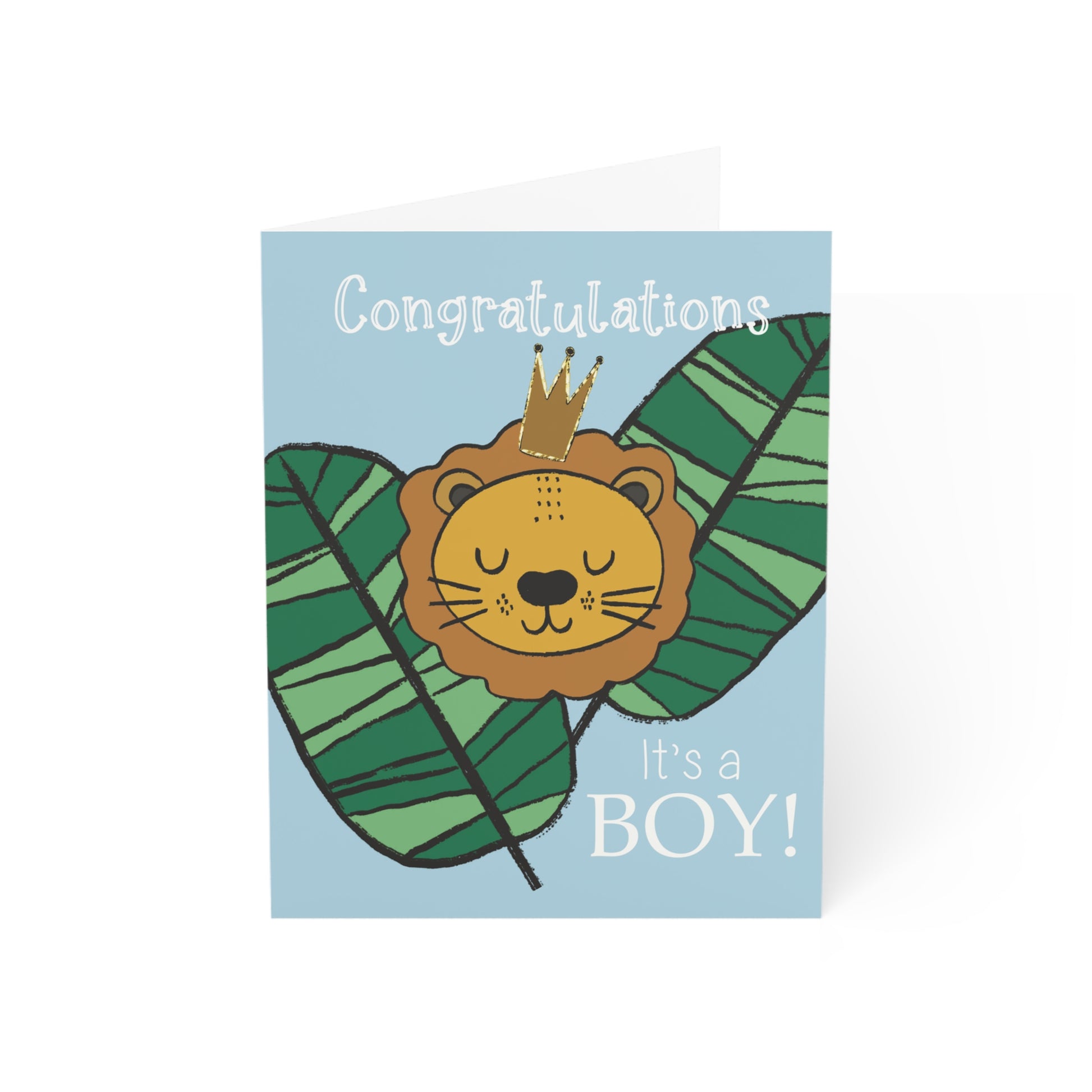 Card shows a powder blue card with 2 vibrant green jungles leaves and a lions cartoon face. He is wearing a little crown and looks peaceful and sleeping. The words in white say “ Congratulations at the top and It’s a boy! At the bottom