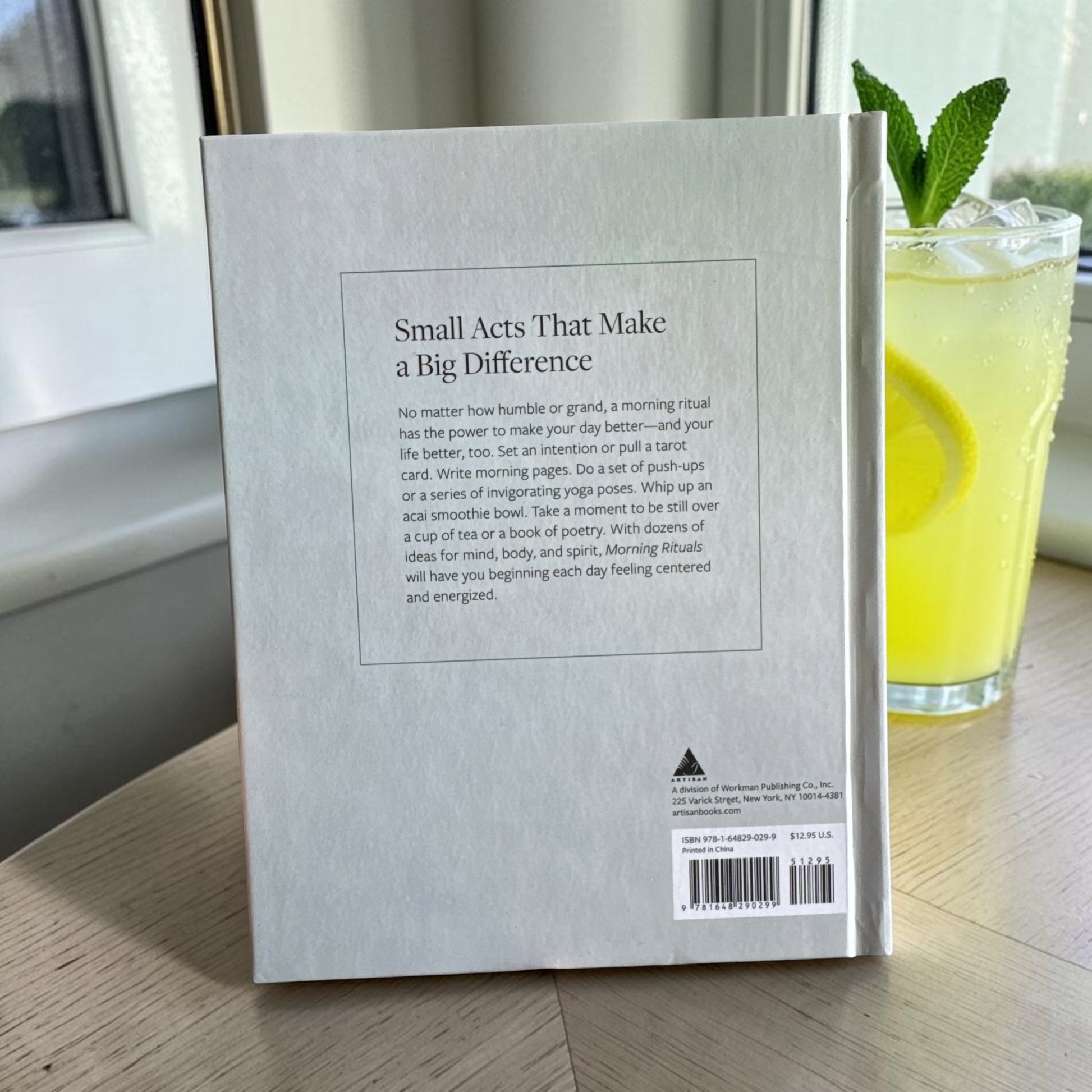 Book titled 'Small Acts That Make a Big Difference' on a surface with a glass of ice lemonade in the background.