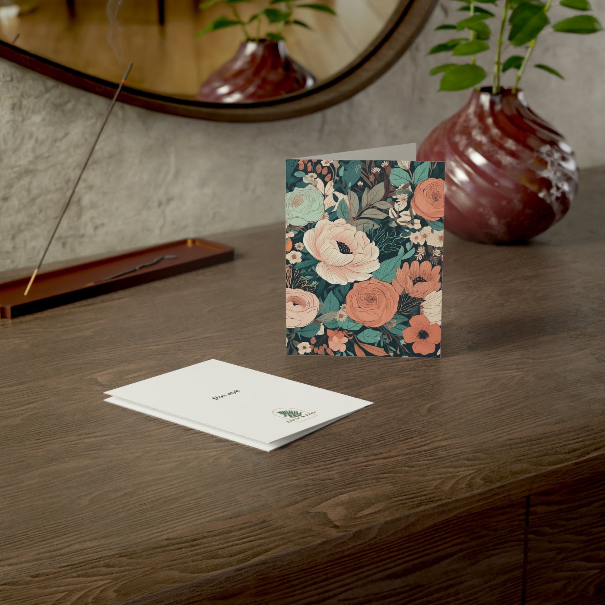 Front of a greeting card featuring a moody, Regency-inspired floral pattern in shades of pink, coral, light blue, and cream, set against a rich teal background. The elegant design evokes the romantic and refined aesthetic of the Regency era, with delicate blooms creating a timeless and sophisticated look. The inside of the card is blank, perfect for personal messages, and the back includes the text 'Blank inside' along with the company logo.