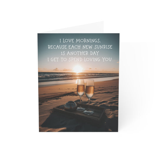 A romantic greeting card featuring a sunrise, two glasses of champagne on a beach blanket, and the message "I love mornings, because each new sunrise is another day I get to spend loving you.