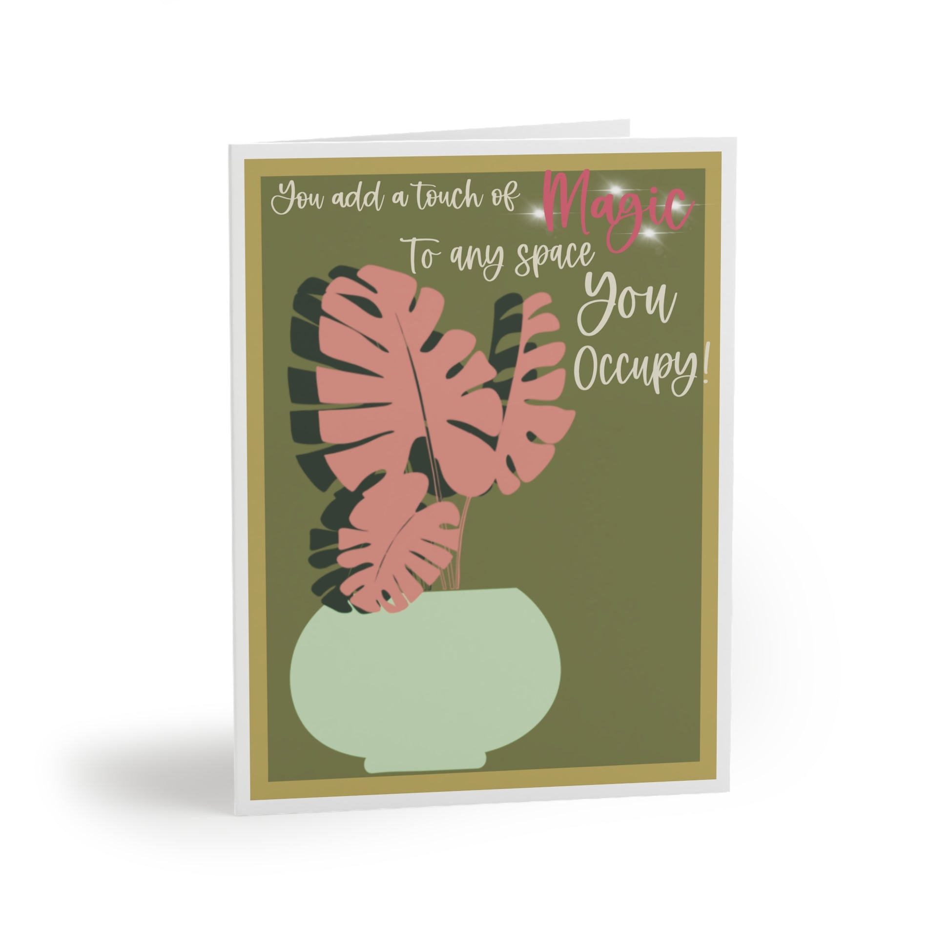 Front of a sage green greeting card with a white border, featuring a mint-colored pot holding a unique pink Monstera plant. The card includes the phrase 'You add a touch of magic to every space you occupy' written in pink, adding a heartfelt message. The card's blank inside is perfect for a personalized note, with the back displaying the text 'Blank inside' and the company logo.