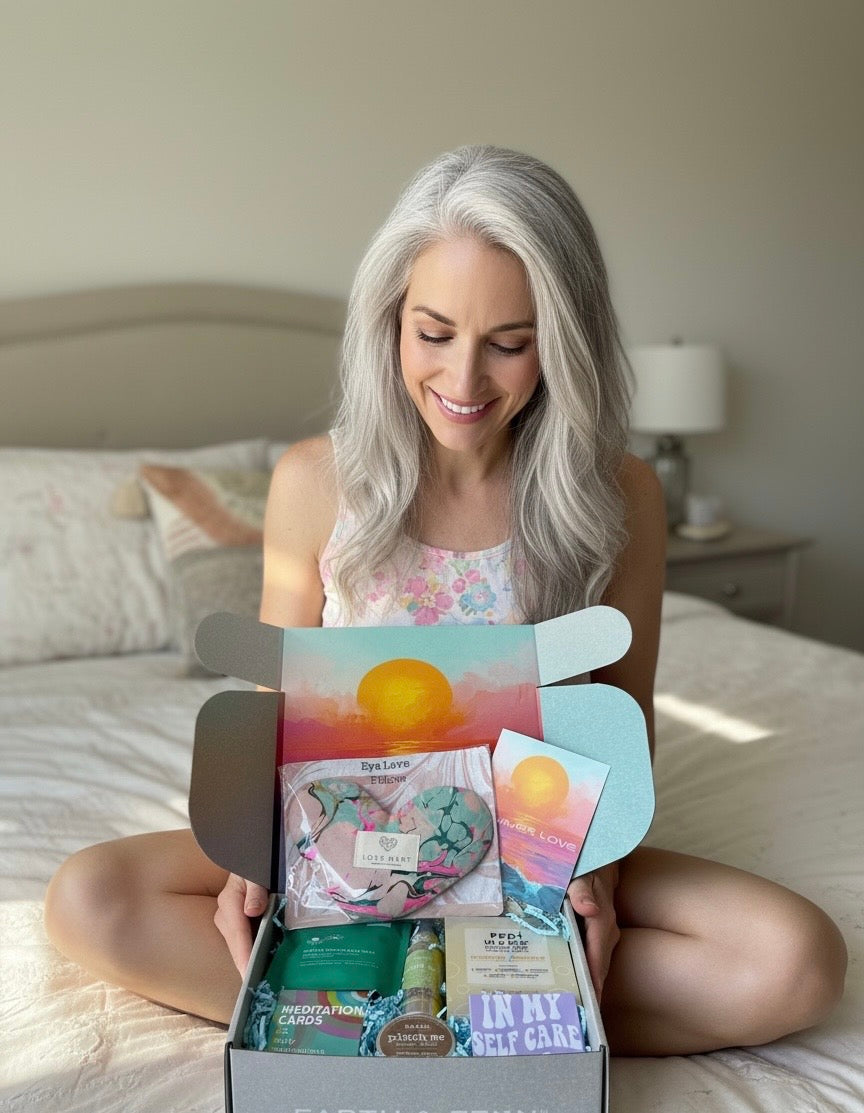 Woman sitting on a bed smiling and holding an open wellness box of Summer Love self-care items.