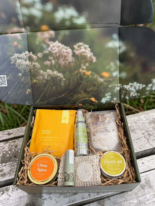 Open sunshine garden box, with bath soaks, therapy dough, candle, face mist, lip balm. All in bright happy citrus colors with hints of green. 