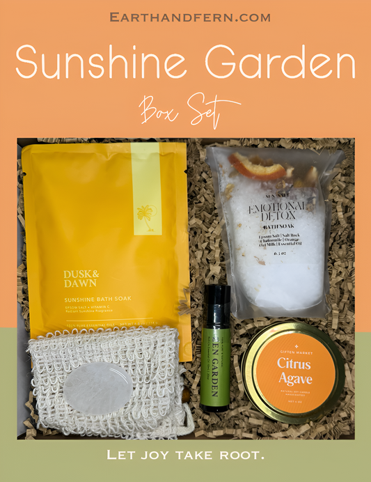 Bright and cheerful wellness gift box called Sunshine Garden, featuring a citrus agave soy candle, citrus peel bath soak, sunshine epsom salt soak, essential oil roll-on, and a clear quartz crystal, arranged in a vibrant yellow, orange, and melon  green color theme.
