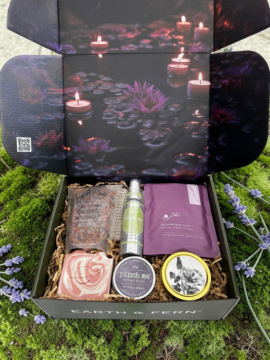 Open box with Midnight Mood and Dusk to Dawn bath soaks, Aromatherapy Spray for on the go, Therapy dough in lavender, hibiscus patchouli candle, and luxurious lavender rose soap, with complimentary sisal soap bag.