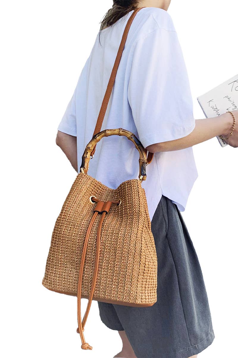 Boho-style woven rattan bucket bag with bamboo top handle and crossbody strap, featuring drawstring closure and inner compartments 