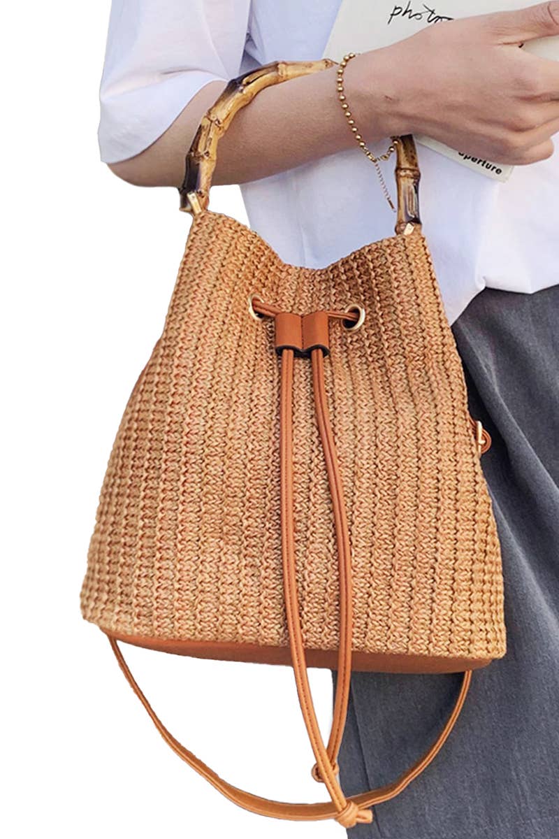 Boho-style woven rattan bucket bag with bamboo top handle and crossbody strap, featuring drawstring closure and inner compartments
