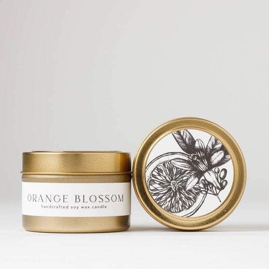 Hand-poured 4 oz. soy candle from the Flora Collection with sweet orange, clementine leaves, neroli, and water lily, in a clear glass jar with a gold steel lid.