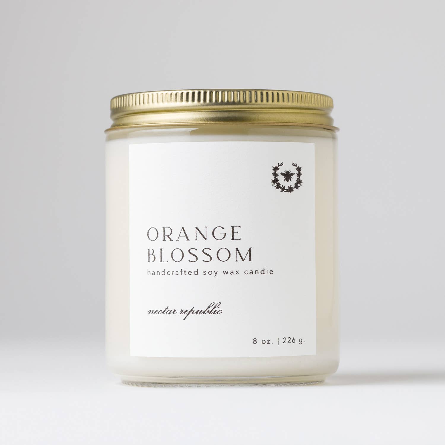 Hand-poured 8 oz. soy candle in Orange Blossom from the Flora Collection with notes of sweet orange, clementine leaves, neroli, and water lily, in a clear glass jar with a gold steel lid. 