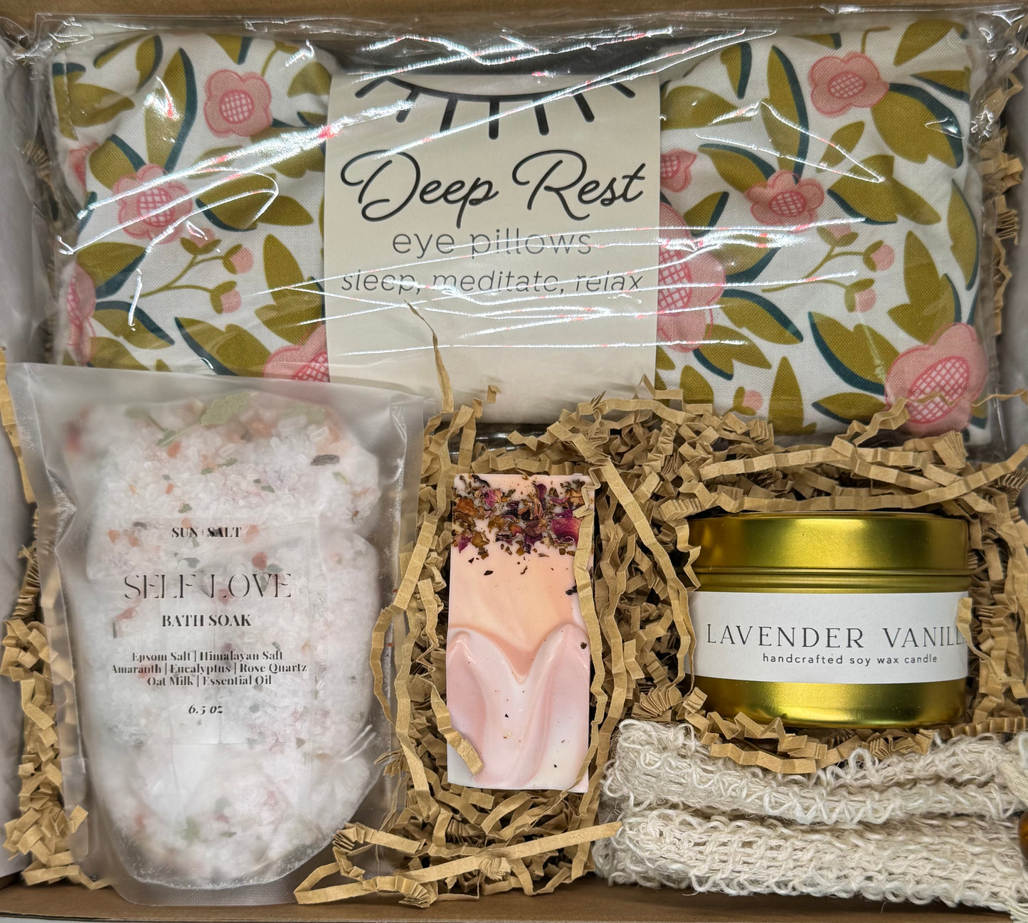 Self-care wellness gift box with lavender vanilla candle, handcrafted lavender rose soap, bath tea soak, and warm-cold therapie face pillow for relaxation and stress relief.
